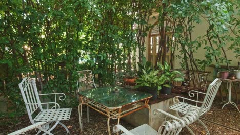 Gartenmöbel-Mit-Weißen-Stühlen-Und-Einem-Glastisch-Unter-Grünen-Bäumen-In-Einem-Sommerlichen-Hinterhof