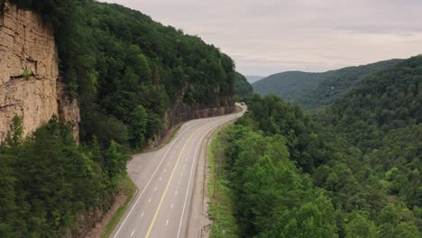 cinematic-ariel-of-a-long-and-windy-american-road-in-the-countryside-with-large-trucks-and-cars-passing-through-the-shot-on-a-hot-and-muggy-afternoon-in-the-mountains-of-west-virginia