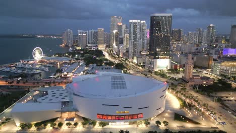Estadio-Del-Centro-De-Baloncesto-Del-Centro-De-Miami,-Florida-Y-Noria-Con-El-Horizonte-De-La-Ciudad-Al-Atardecer,-Luces-Brillantes