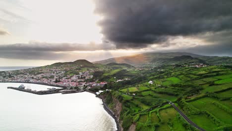 Aufsteigende-Drohnenaufnahme-Der-Insel-Faial-Auf-Den-Azoren-Bei-Sonnenuntergang-Mit-Grüner-Vegetation-Und-Der-Stadt-Horta-Im-Hintergrund