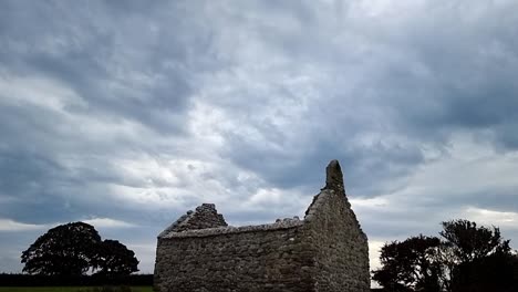 The-ruins-of-Capel-Lligwy-on-rural-Moelfre-countryside,-Anglesey,-North-Wales,-Tilting-down-shot