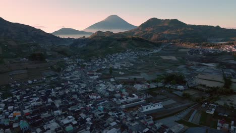 Cinematic-drone-flight-over-rural-landscape-with-village-in-valley-and-mountain-range-in-background-during-sunny-day-in-Indonesia
