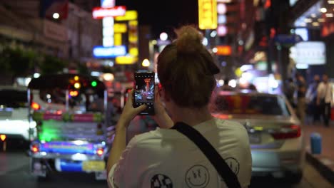 Female-Traveler-Stops-To-Take-A-Photo-Of-The-Colorful,-Energetic,-And-Vibrant-Night-Scenes-Of-Bangkok-Thailand-After-Dark