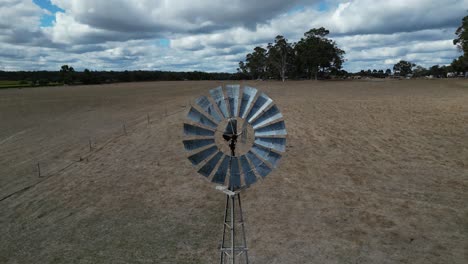 Aerial-backwards-shot-of-rotating-windmill-on-farm-field-during-cloudy-day-,-Margaret-River-Region