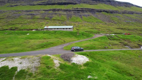 Drohne-Verfolgt-Ein-Auto,-Das-Auf-Einer-Von-Bergen-Und-Wasserfällen-Umgebenen-Straße-Nach-Saksun-Auf-Den-Färöer-Inseln-Fährt