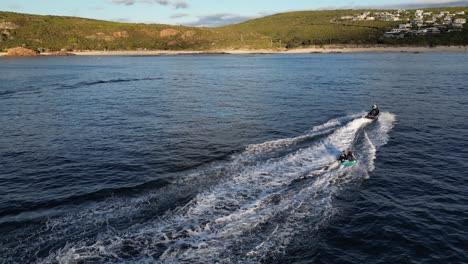 Slow-motion-drone-shot-of-jet-ski-carrying-inflatable-boat-with-people-having-fun-on-ocean