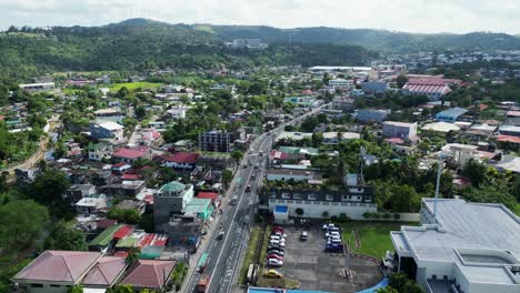 Rising-drone-shot-of-bustling-town-center-in-Legazpi,-Albay-with-busy-roads,-buildings,-and-mountains-in-background