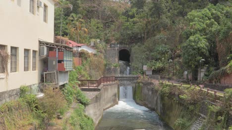 Ein-Wasserfall,-Der-Wasser-Von-Der-Seite-Eines-Hügels-In-Einen-Kanal-In-Einem-Kleinen-Dorf-Im-Süden-Taiwans-Spritzt-–-Totale