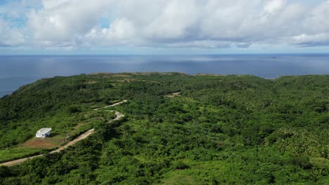 Aerial-drone-shot-overlooking-vast-island-jungle-with-serpentine-road-facing-turquoise-ocean-bay-and-cloudscape-in-Pandan,-Catanduanes