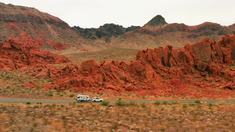 Aerial-view-of-a-truck-with-trailer-driving-on-a-road-in-middle-of-red-rocks-in-Nevada,-USA
