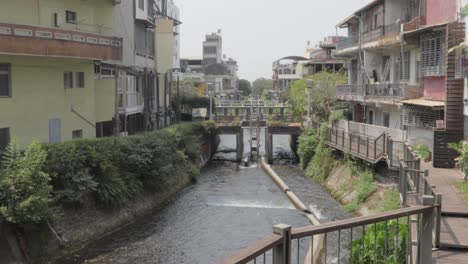 Ein-Fluss,-Der-Durch-Einen-Kanal-Mit-Dreistöckigen-Gebäuden-Auf-Beiden-Seiten-In-Einem-Kleinen-Dorf-Im-Süden-Taiwans-Fließt-–-Breit