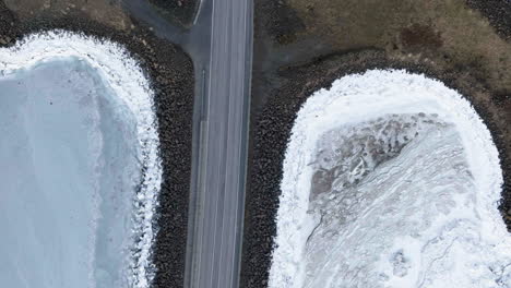 Aerial-top-shot-above-cars-driving-in-frozen-nature,-sunny-winter-day-in-Iceland