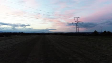 Drohnenaufnahme-Einer-Wunderschönen-Aussicht-Auf-Den-Sonnenuntergang-Von-Der-Farmlandschaft-Mit-Einem-Hochspannungsmast