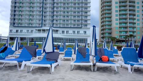 Liegestuhl-Und-Sonnenschirm-Am-Strand-Zur-Touristischen-Entspannung-Mit-Hotelgebäude-Im-Hintergrund