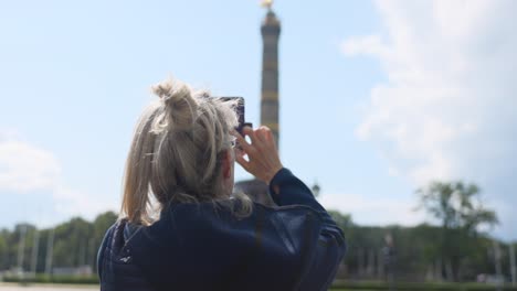 Mujer-Caucásica-Tomando-Una-Foto-Con-Un-Teléfono-Celular-De-La-Columna-De-La-Victoria-De-Berlín