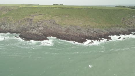 Ocean-Waves-Crashing-On-Rocky-Cliffs-In-Ballycotton,-County-Cork,-Ireland---aerial-pullback