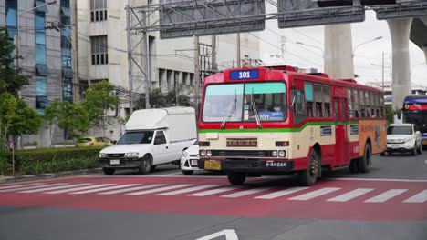 Public-Local-Red-Bus-Passing-Through-A-Crosswalk-In-Bangkok,-Thailand