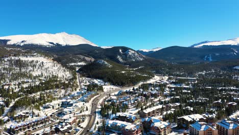 Beautiful-Breckenridge-Colorado-Mountain-Town-Aerial-Drone-View-of-Snow-Covered-Houses-and-Mountains-with-People-Driving-on-Road-Through-Pine-Tree-Forest
