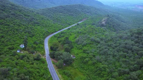 Vista-Aérea-De-Un-Camino-A-Través-De-Un-Bosque-Exuberante-Selva-Verde-Con-Un-Telón-De-Fondo-Montañoso-Durante-El-Monzón-En-Gwalior-Madhya-Pradesh-India