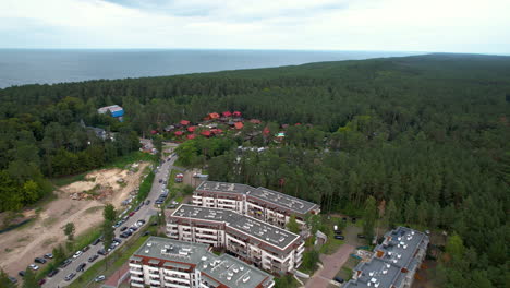 Aerial-forward-flight-over-polish-district-with-houses-and-traveling-cars-and-forest-landscape-with-sea-in-Stegna,-Poland