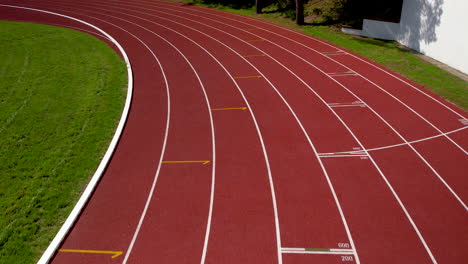 Aerial-forward-flight-over-empty-red-running-track-in-stadium-at-summer-day