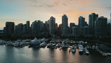 Drone-flight-over-marina-with-yachts-and-beautiful-skyline-of-Vancouver-in-background-at-sunset---British-Columbia,-Canada