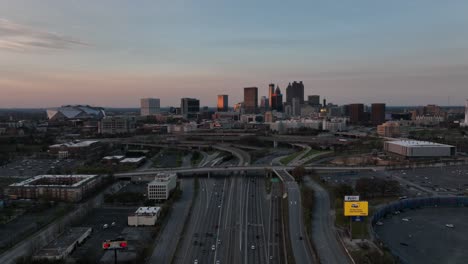 Autopista-Del-Centro-De-Atlanta,-Intercambio-Con-El-Icónico-Horizonte-Y-Rascacielos-En-El-Fondo-Bajo-El-Cielo-Del-Atardecer,-Vista-Aérea