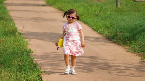 Stylish-Confident-Little-Girl-in-Pink-Dress-and-Sunglasses-Walks-in-a-Park-Down-the-hill-on-Summer-Day
