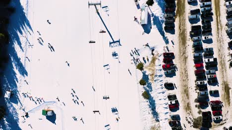Busy-Ski-Slope-with-People-Riding-Cairlift-next-to-Full-Parking-Lot-and-Crowded-Trail