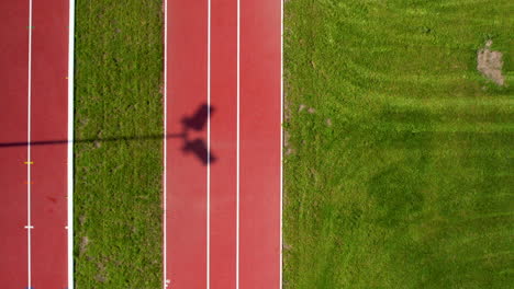Aerial-top-down-shot-of-running-track-between-grass-field-in-Stadium-during-sunny-day---flyover