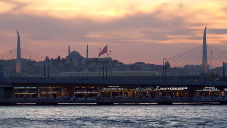 Goldene-Horn-U-Bahn-Brücke-Bei-Sonnenuntergang-Mit-Einer-Moschee-Im-Hintergrund,-Istanbul,-Türkei