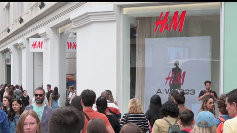 Compradores-Y-Peatones-Pasan-Por-La-Multinacional-Sueca-De-Diseño-De-Ropa,-La-Empresa-Minorista-Hennes-Y-Mauritz,-Tienda-H&amp;M-En-España