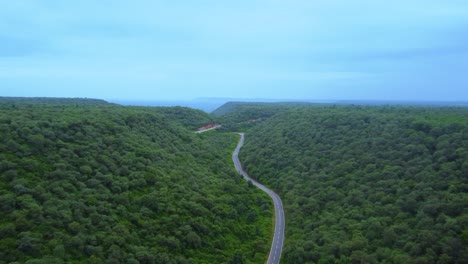 Luftdrohnenaufnahme-Eines-Motorrads-Auf-Einer-Forststraße-Durch-üppigen-Grünen-Dschungel-Mit-Hügeliger-Kulisse-Während-Des-Monsuns-In-Gwalior,-Madhya-Pradesh,-Indien