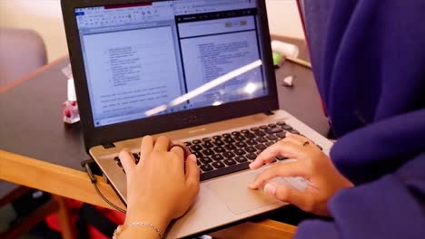 Back-view-close-up-of-female-student-sitting-at-desk-at-home-looking-at-laptop-screen-typing,-focused-millennial-female-student-busy-studying-away-on-computer,-filling-out-documents-on-gadget