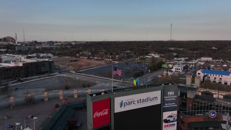 Die-Drohne-Kreist-Um-Die-Nationalflagge-Der-Vereinigten-Staaten-Von-Amerika-Und-Zeigt-Bei-Sonnenuntergang-Ein-Leeres-Georgia-State-Stadium