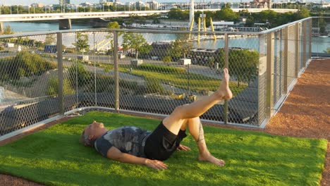 Man-is-doing-Exercises-on-a-modern-terrace-in-Vienna,-with-the-beautiful-Danube-Island-in-the-back,-4K