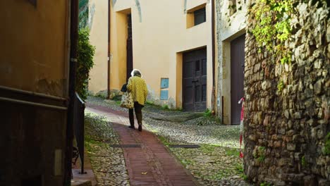 Old-Woman-Walking-On-Paved-Walkway-In-Spoleto,-Umbria,-Italy