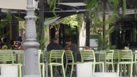 Dos-Hombres-Sentados-En-Un-Comedor-Al-Aire-Libre-Esperando-Su-Comida.