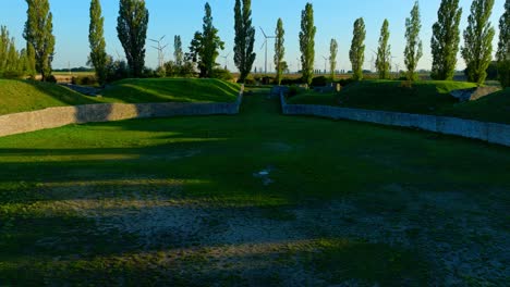 Flying-Over-The-Carnuntum-Amphitheatre-Towards-The-Trees-Near-The-Wind-Farm