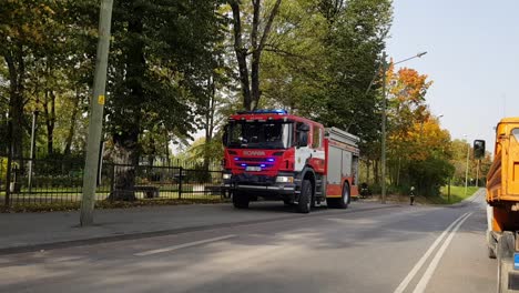 Red-Scania-firetruck-with-lights-on-next-to-the-road-cars-drive-by