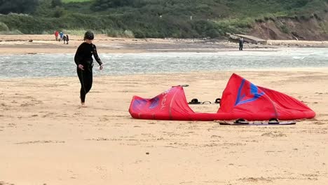 Aktives-Kitesurf-Paar-Bereitet-Wassersportausrüstung-Am-Windigen,-Bewölkten-Strand-In-Wales-Vor