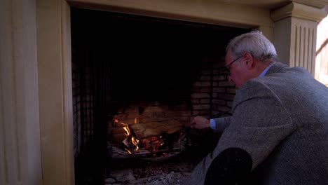 Slow-motion-shot-of-a-senior-man-using-a-poker-to-move-around-wood-in-a-fireplace