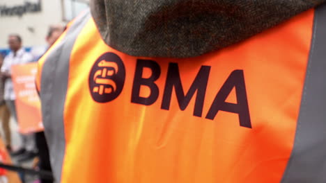 Ein-Streikender-Arzt-Trägt-Einen-Orangefarbenen-Wappenrock-Der-British-Medical-Association-Auf-Einer-Streikpostenlinie-In-Zeitlupe