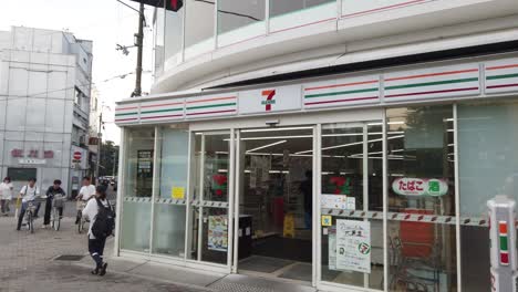 7-Eleven-Convenience-Store-Entrance-Shop,-People-Walk-By-Streets-in-Kyoto-Japan