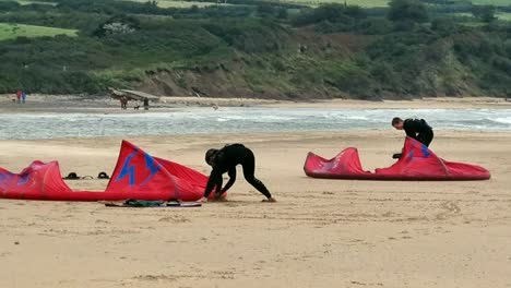 Aktives-Kitesurf-Paar-Bereitet-Freestyle-Wassersportausrüstung-Am-Stürmischen,-Bewölkten-Strand-In-Wales-Vor