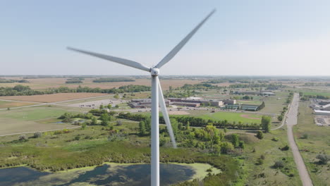Luftaufnahme-Einer-Sich-Drehenden-Windkraftanlage-Mit-Ländlicher-Amerikanischer-High-School-Im-Hintergrund,-Konzept-Der-Bildung-Durch-Erneuerbare-Energien