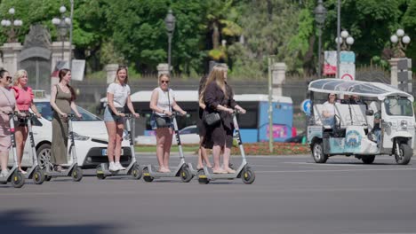Slow-motion-scene-where-teenage-girls-drive-through-traffic-on-electrical-scooters