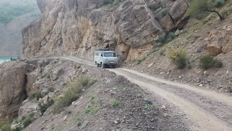 Antigua-Furgoneta-Todoterreno-Uaz-Soviética-Que-Se-Desplaza-Por-Una-Carretera-Polvorienta-En-Un-Paisaje-Desértico-Y-Una-Montaña-De-Asia-Central