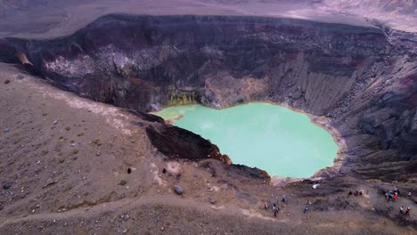 Hot-volcano-crater-lake-aerial-retreats,-reveals-people-on-caldera-rim
