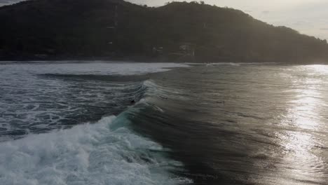 Surfer-rides-big,-pushy-shore-break-surf-wave-in-golden-dusk-lighting